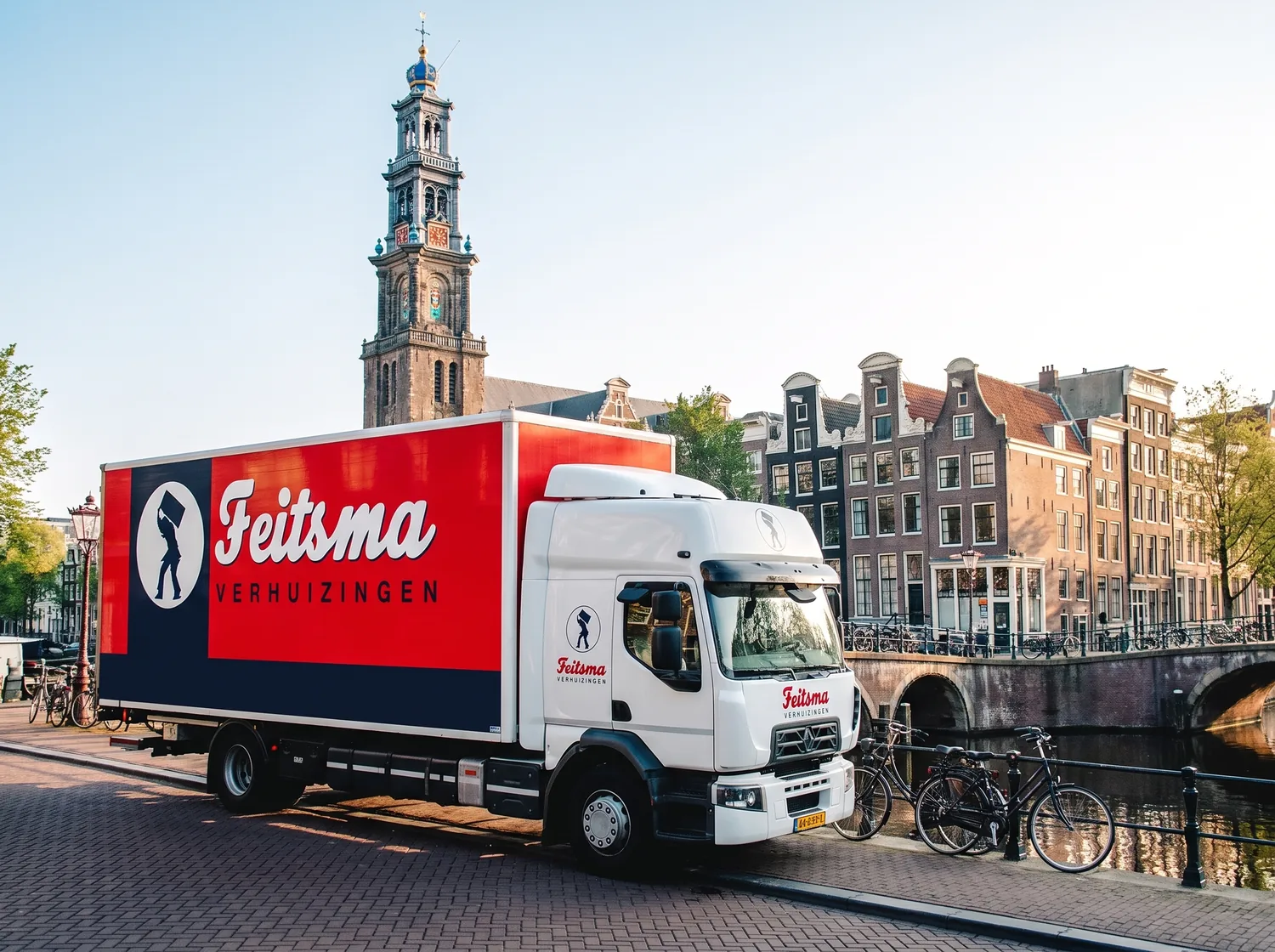 Verhuiswagen van Feitsma aan een Amsterdamse gracht, met de Westertoren en grachtenpanden erachter