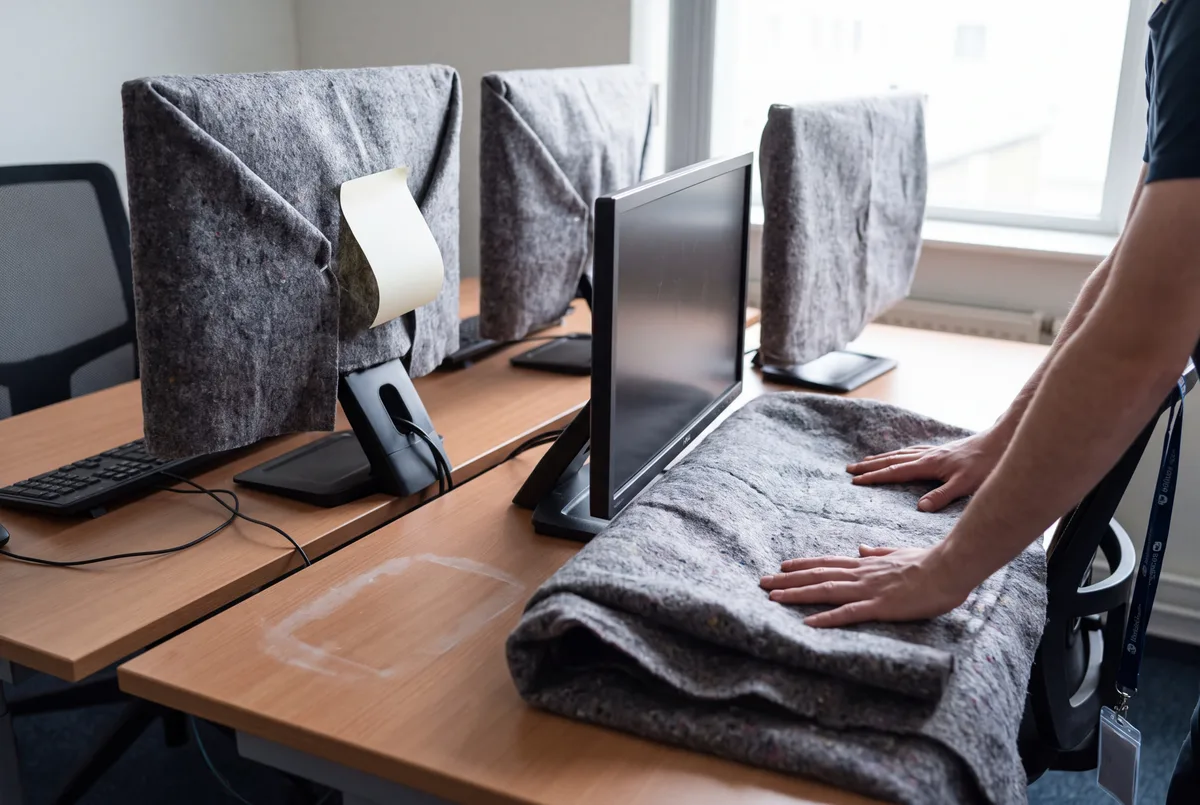 Beeldschermen in verhuisdekens klaargezet op een bureau