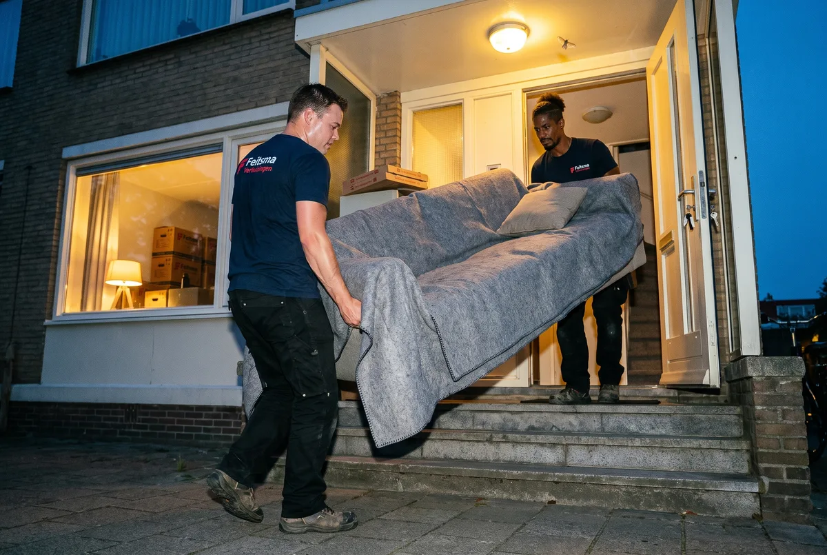 Verhuizers dragen de laatste bank naar binnen in het blauwe uur