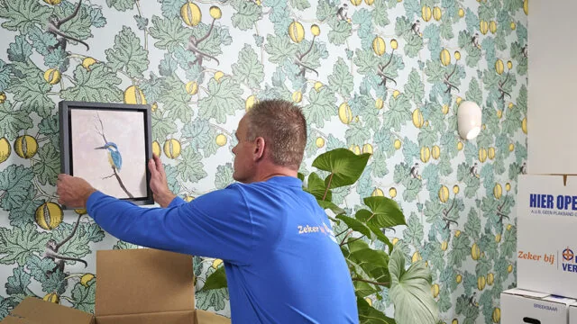 Verhuizer van de campagne van Erkende Verhuizers hangt een schilderij op in de nieuwe woning