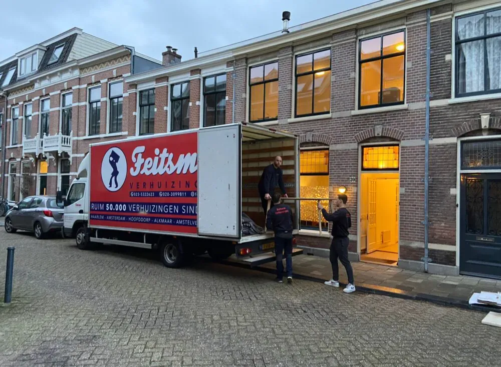 Verhuizers van Feitsma dragen meubels een Haarlemse woning binnen, de wagen staat voor de deur
