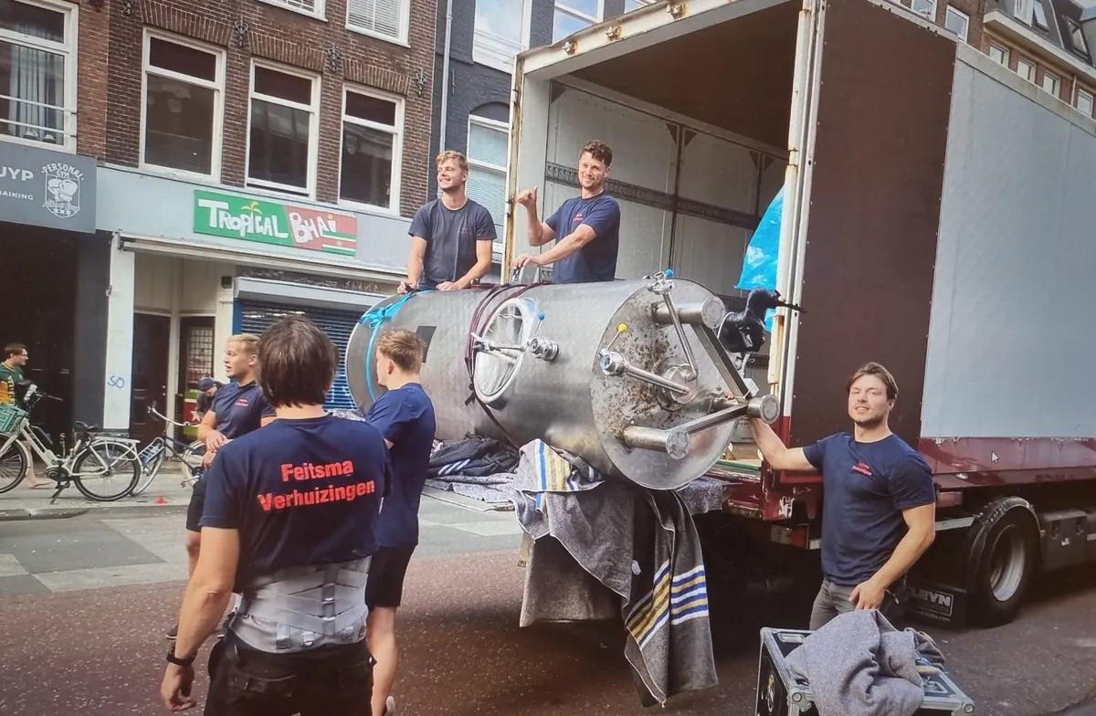 Ploeg van Feitsma tilt een zware stalen ketel de verhuiswagen in op een Amsterdamse straat